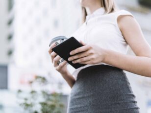 low-angle-view-businesswoman-holding-smartphone-disposable-coffee-cup-outdoors